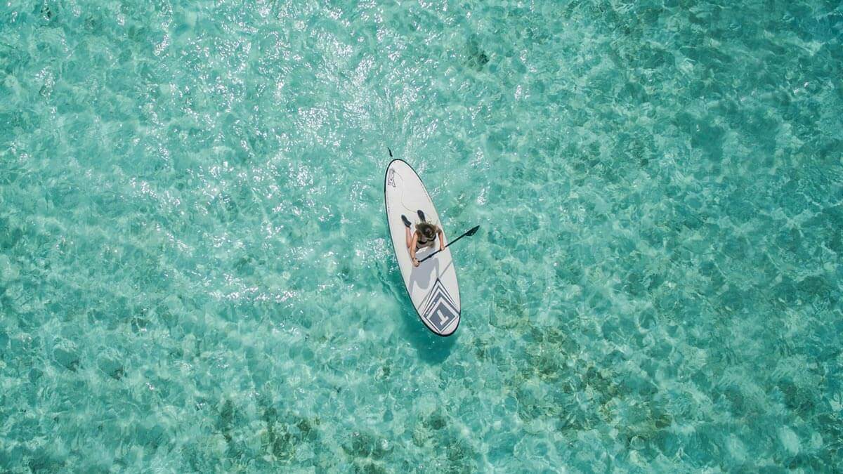 An aerial of a person stand-up paddleboarding on the turquoise lagoon of The Nautilus Maldives