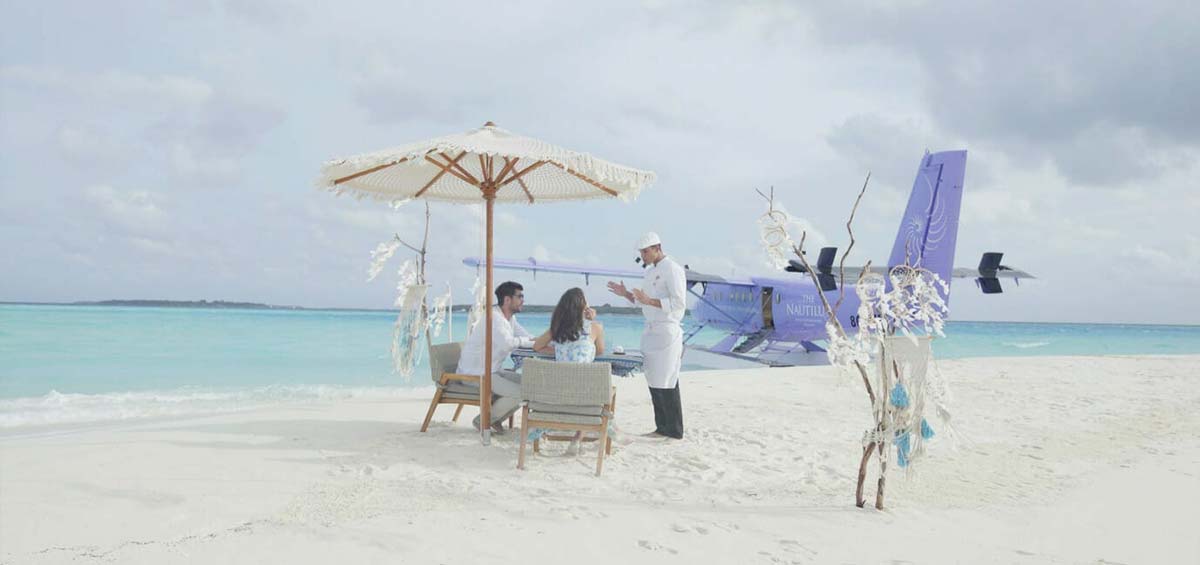 Couple with a chef on a sandbank with set up, and The Nautilus private seaplane docked