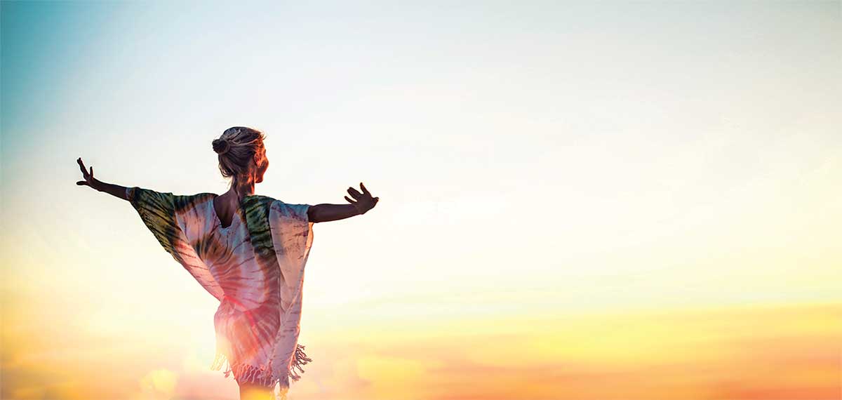 A woman with her arms out and smiling as the sun sets