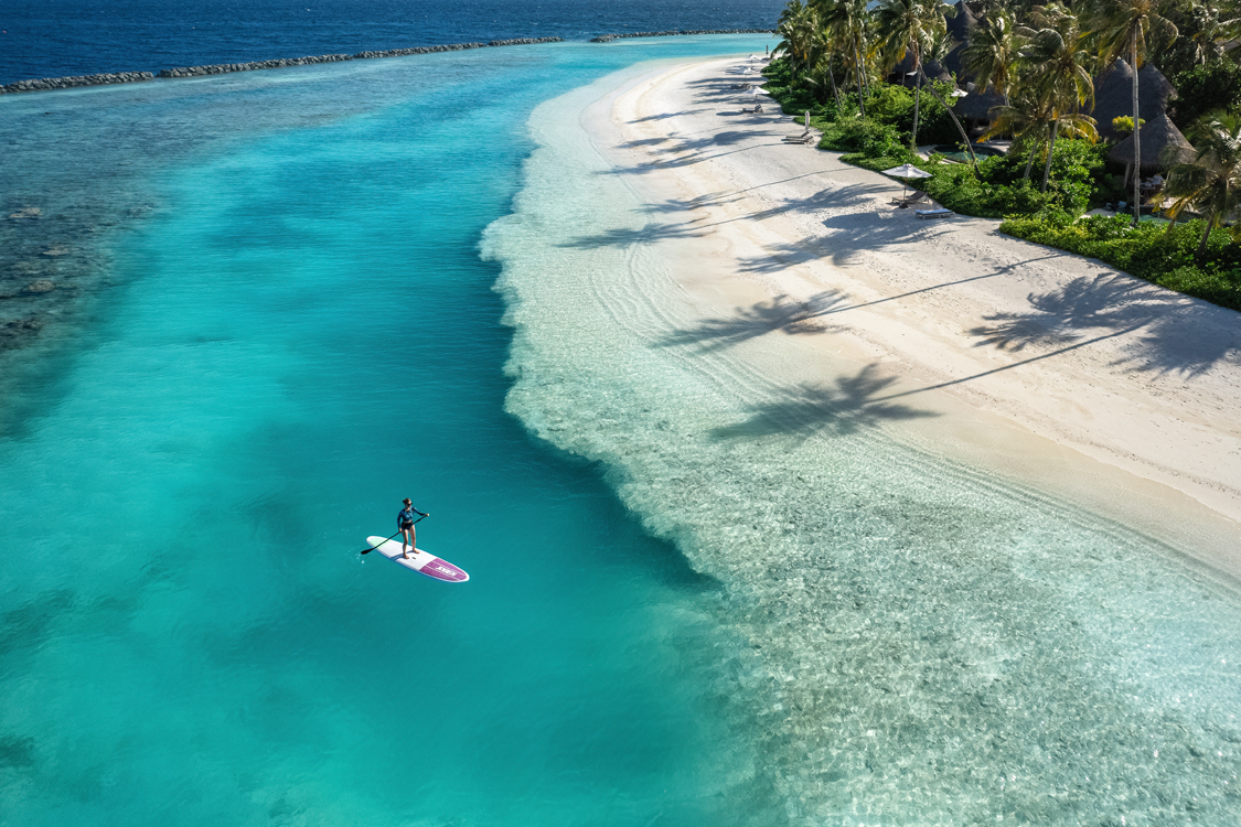 An aerial of a person stand-up paddleboarding on the turquoise lagoon of The Nautilus Maldives