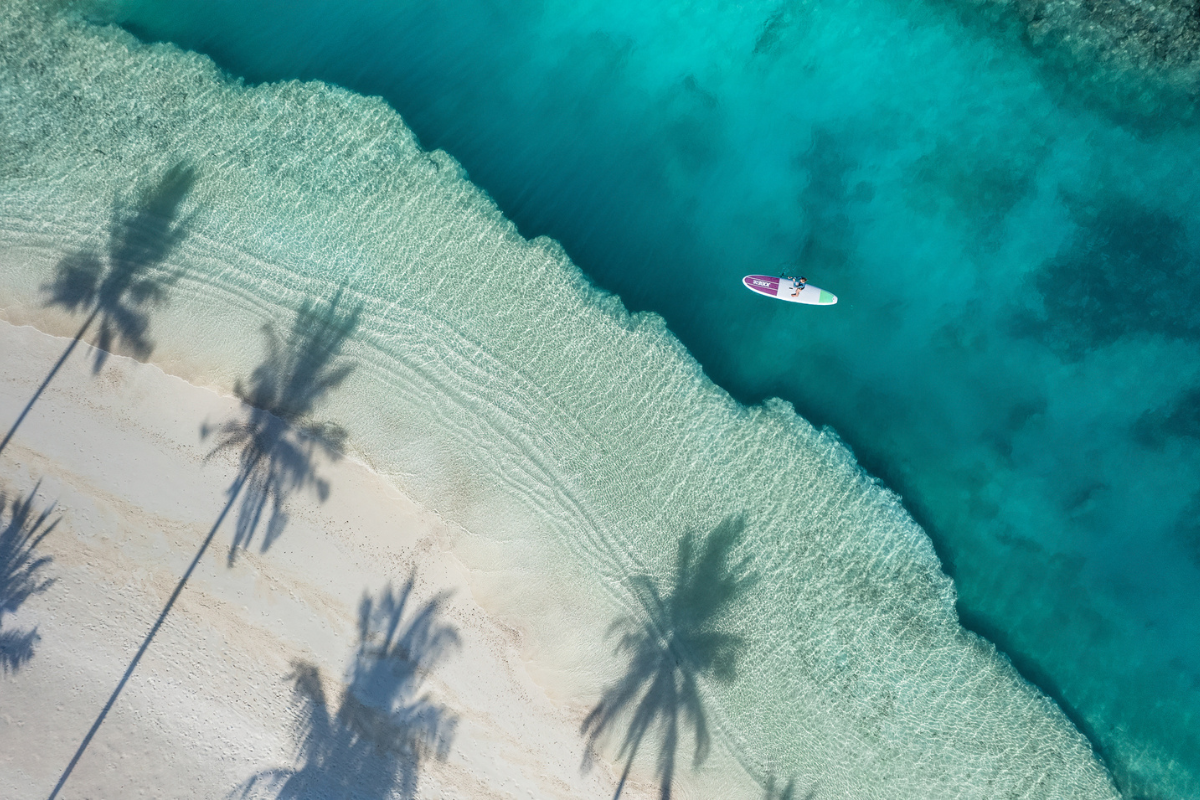An aerial of a person stand-up paddleboarding on the turquoise lagoon of The Nautilus Maldives