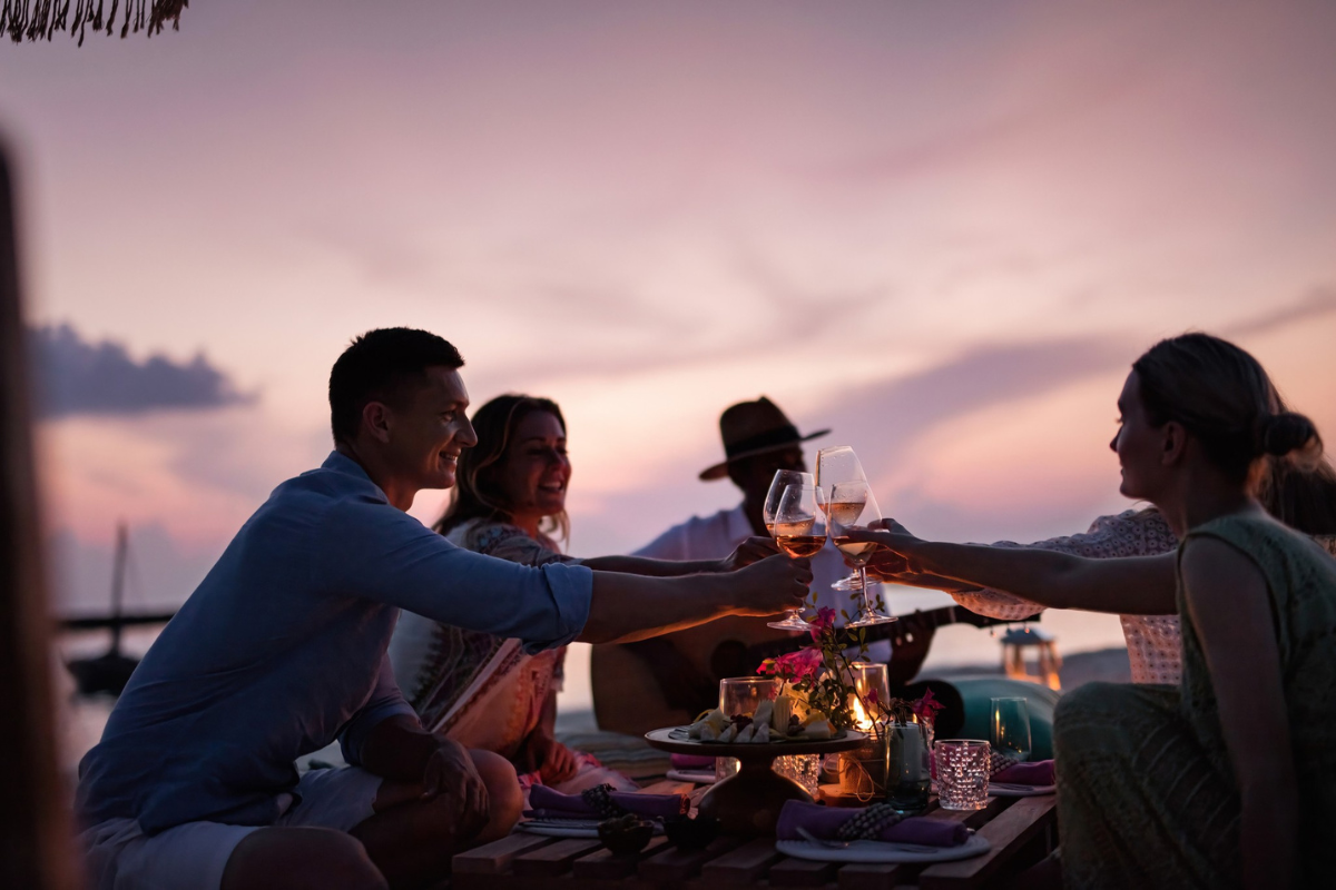 A group of friends toasting with wine on the beach at The Nautilus Maldives