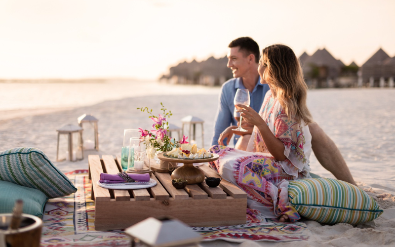 A couple having canapes and champagne on the beach at The Nautilus Maldives