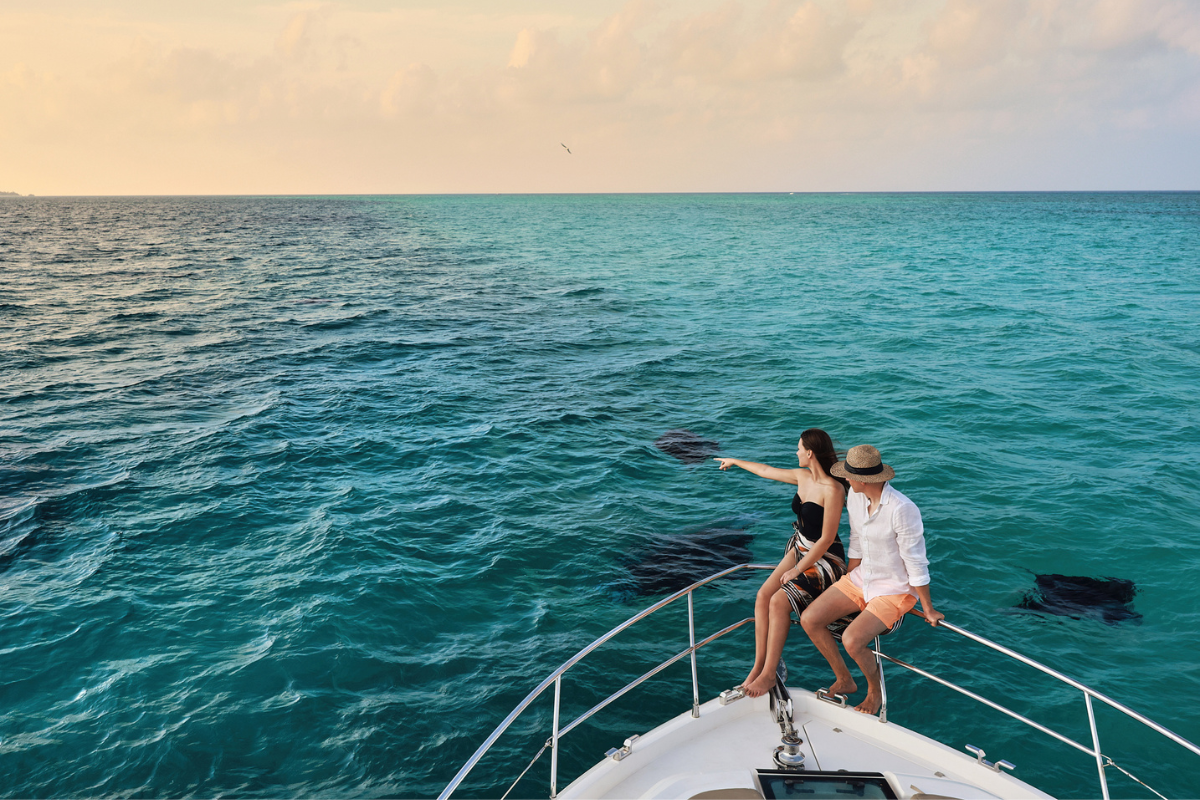 A couple on a luxury yacht looking and pointing at the manta rays in the water