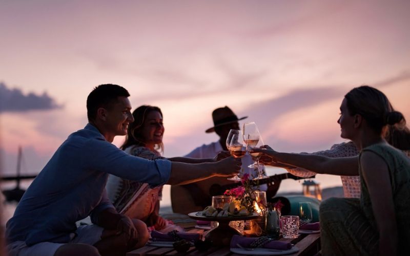 A group of friends toasting with wine on the beach at The Nautilus Maldives