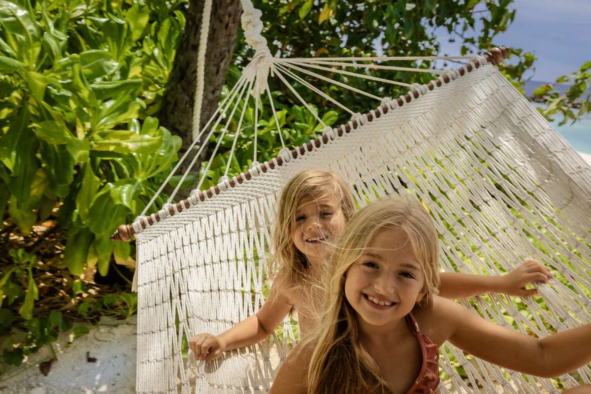 A young boy and girl smiling on a hammock on the beach at The Nautilus Maldives