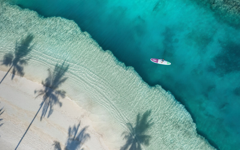 An aerial of a person stand-up paddleboarding on the turquoise lagoon of The Nautilus Maldives