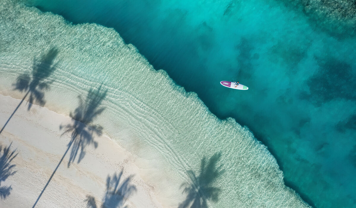 An aerial of a person stand-up paddleboarding on the turquoise lagoon of The Nautilus Maldives