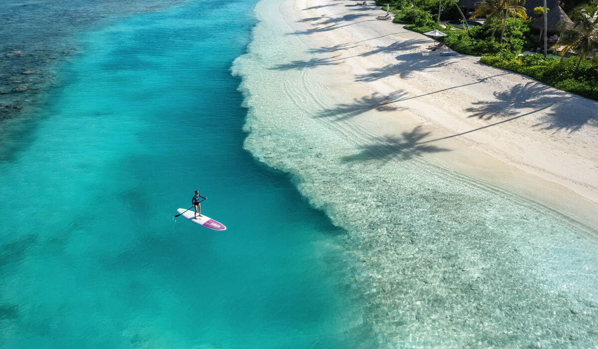 An aerial of a person stand-up paddleboarding on the turquoise lagoon of The Nautilus Maldives