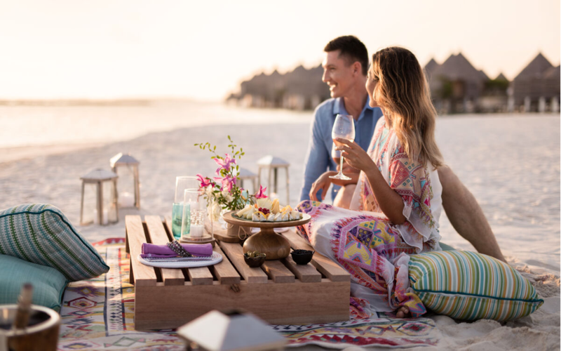 A couple having canapes and champagne on the beach at The Nautilus Maldives