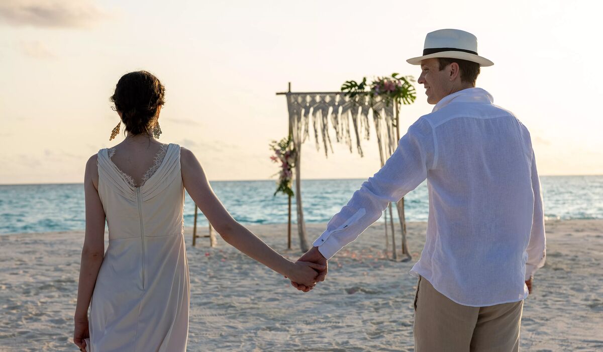 A couple holding hands and walking towards a bohemian-style wedding arch on a sandbank