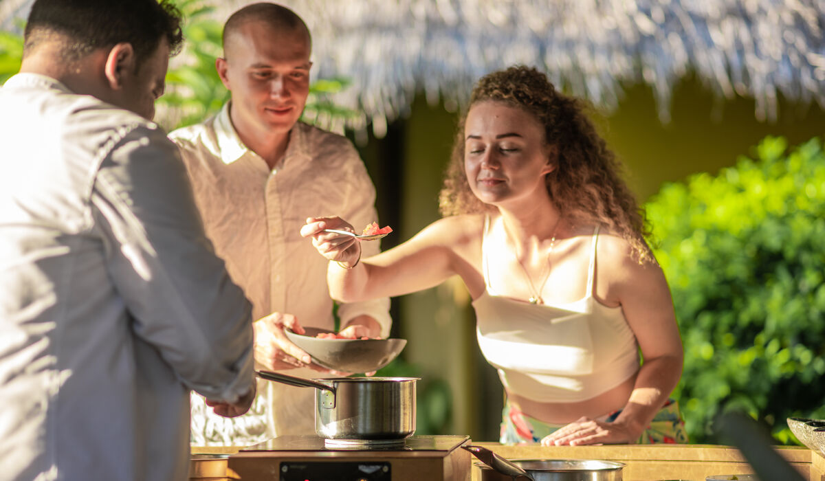 A woman holding up a spoon in front of a chef, savouring the aroma
