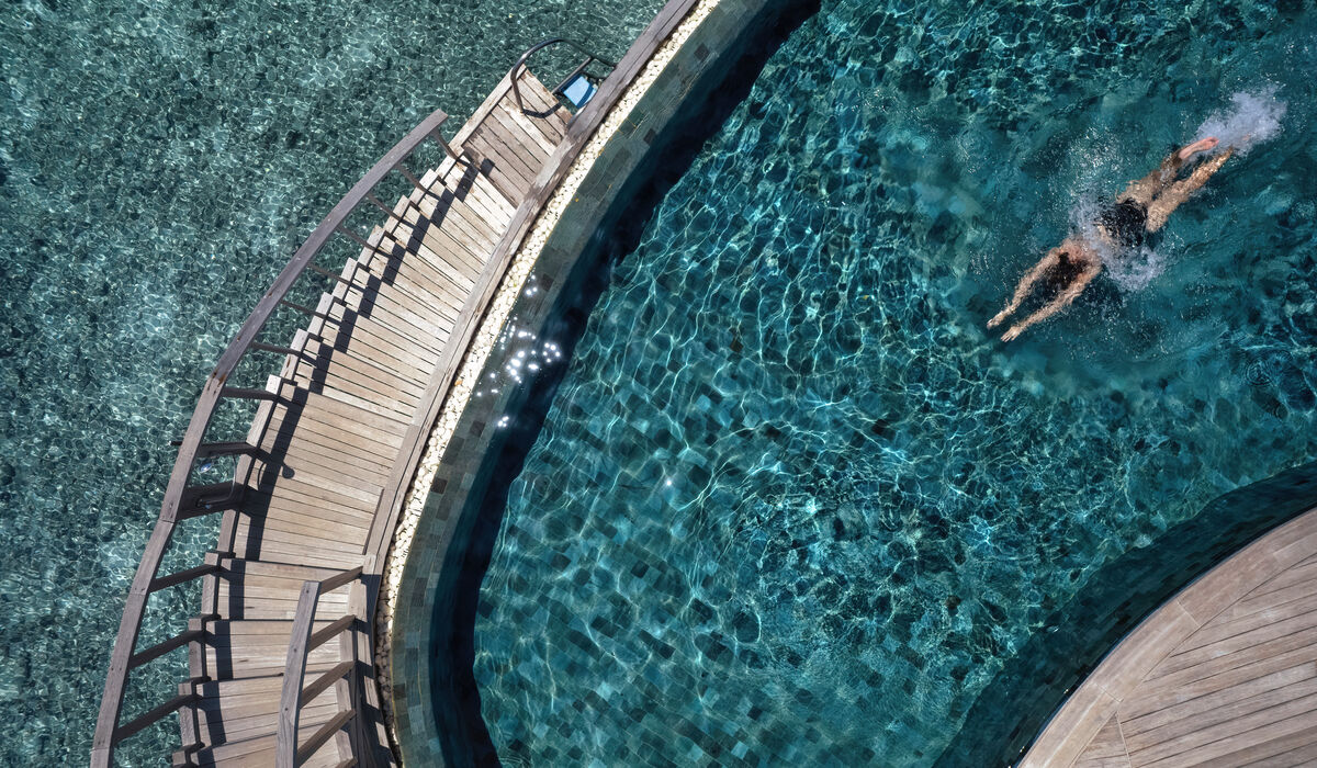 Aerial of a woman diving into the private pool of her ocean house at The Nautilus Maldives
