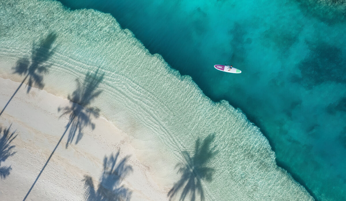 An aerial of a person stand-up paddleboarding on the turquoise lagoon of The Nautilus Maldives