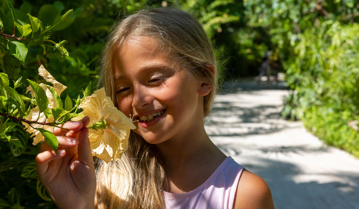 A young girl smiling and holding a hibiscus flower at The Nautilus Maldives