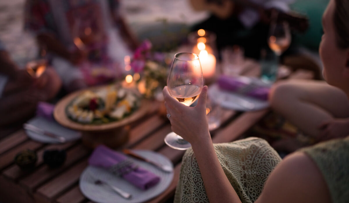 Woman holding up a wine glass at an intimate picnic setup on the beach at The Nautilus Maldives